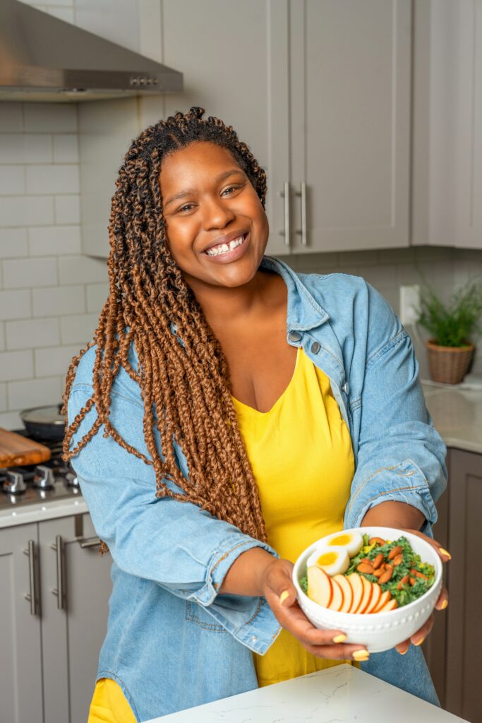 A smiling woman holds a bowl of food in a kitchen